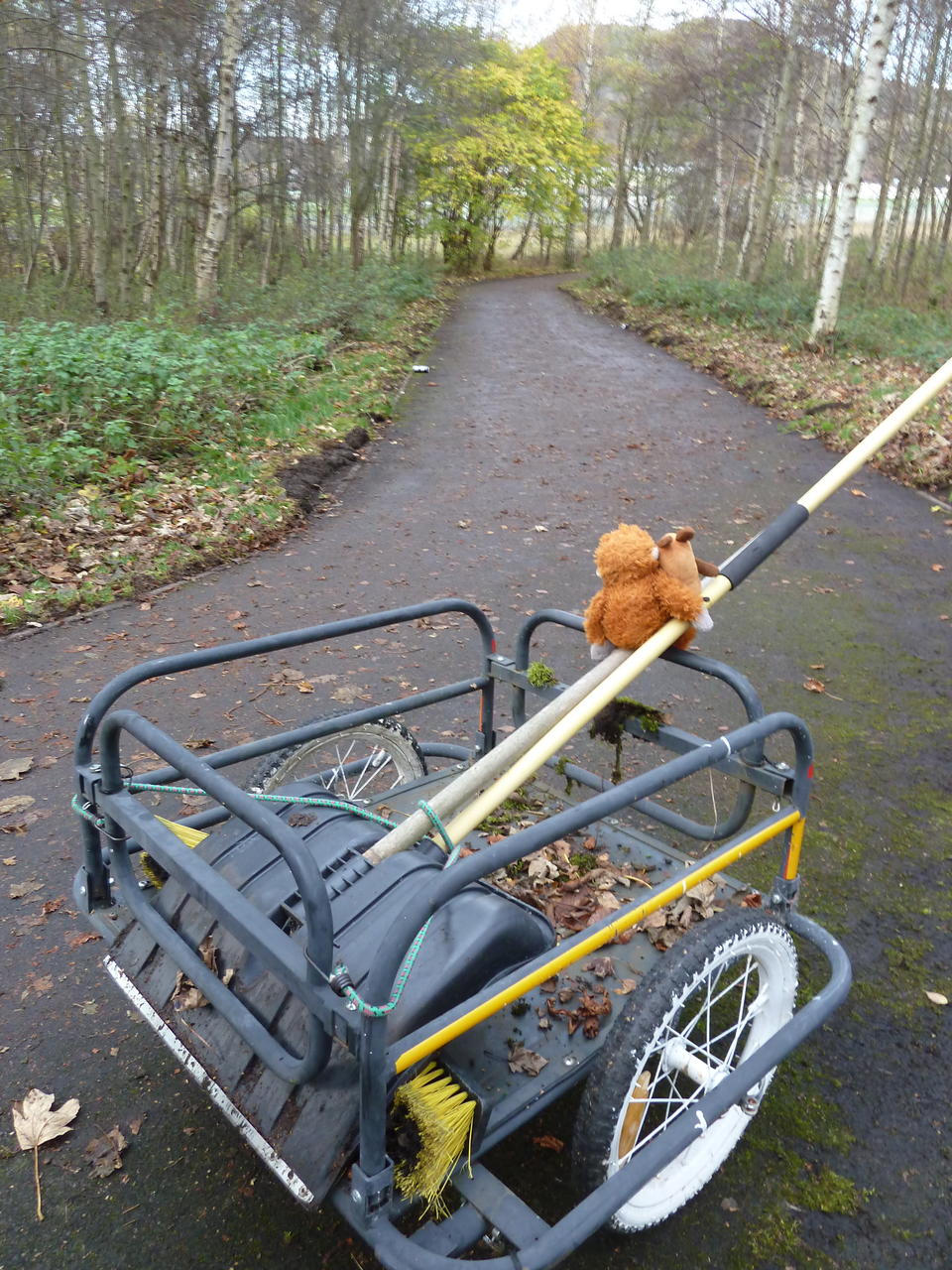 A bicycle trailer with the shovel on it; Mouse and Pongo sit on the shovel and look at the clean path